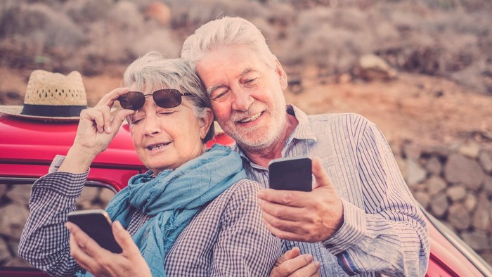 Ein älteres Paar posiert mit Handys an einem Strand.
