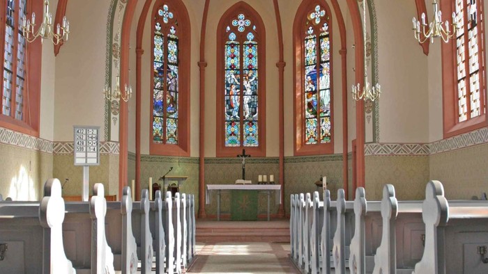 Elegante Kircheninnenausstattung mit Buntglasfenstern, hölzernen Kirchenbänken und einem zentralen Altarbereich.