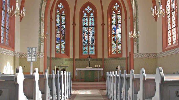Elegante Kircheninnenausstattung mit Buntglasfenstern, hölzernen Kirchenbänken und einem zentralen Altarbereich.