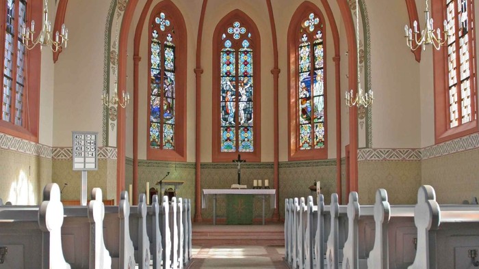 Elegante Kircheninnenausstattung mit Buntglasfenstern, hölzernen Kirchenbänken und einem zentralen Altarbereich.
