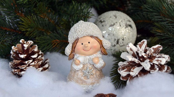 En lille julepige med hvid hat og skøjte, omgivet af granegrene, pinecones og snø.