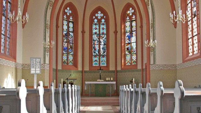 Elegante Kircheninnenausstattung mit Buntglasfenstern, hölzernen Kirchenbänken und einem zentralen Altarbereich.