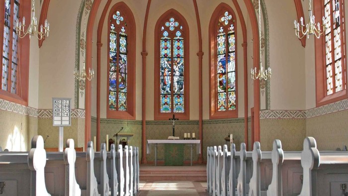 Elegante Kircheninnenausstattung mit Buntglasfenstern, hölzernen Kirchenbänken und einem zentralen Altarbereich.