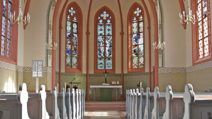 Elegante Kircheninnenausstattung mit Buntglasfenstern, hölzernen Kirchenbänken und einem zentralen Altarbereich.