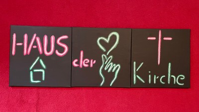 Das Neon-Schild zeigt "HAUS der Liebe Kirche" auf schwarzem Hintergrund