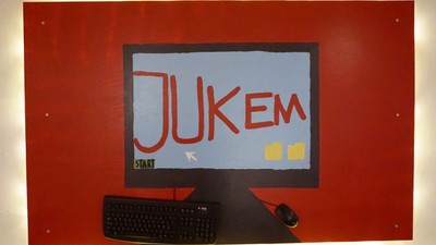 Das Bild zeigt einen roten Monitor mit der Aufschrift "JUKEM" und einer Tastatur davor.