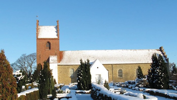 En snede kirke med tårn og hvide vinduer, omgivet af sne og træer