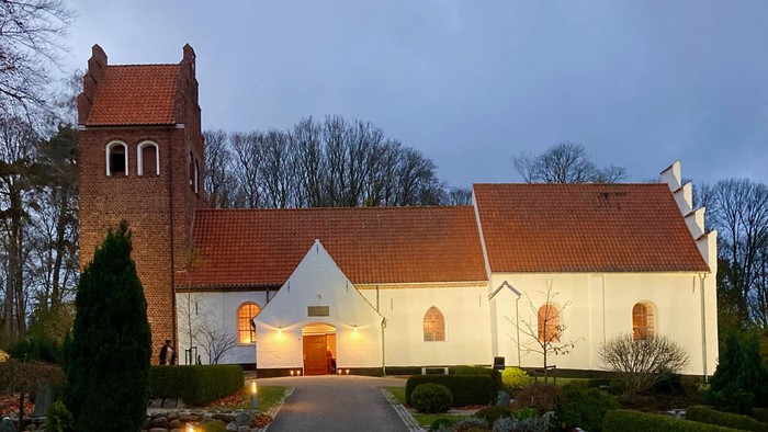 En lille kirke med røde tag og en smal asfaltvej der leder op til den