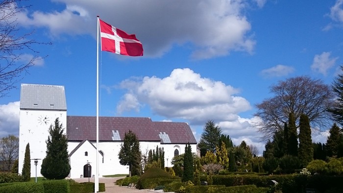 En hvid kirke med dansk flag på en solskinnede dag