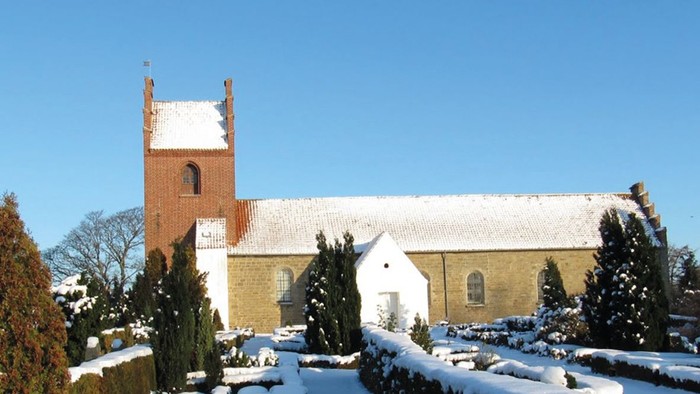 En snede kirke med tårn og hvide vinduer, omgivet af sne og træer