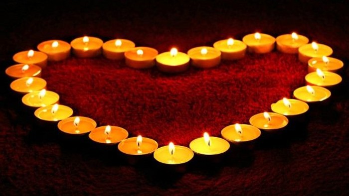 Herzförmige Anordnung von brennenden Kerzen auf rotem Stoff