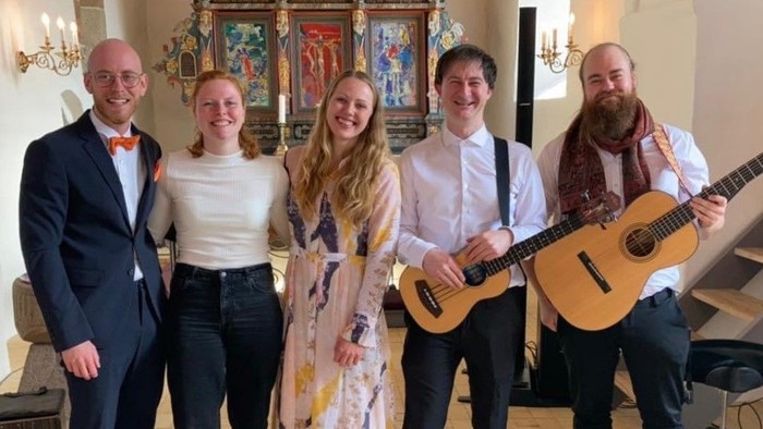 En gruppe af fem personer poser med guitarer i en kirke