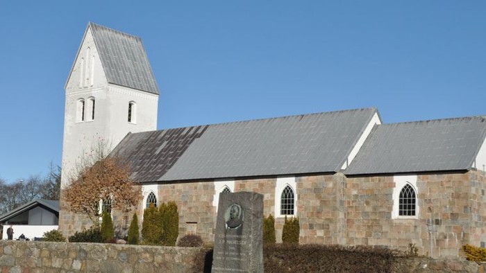 En lille kirke med tårn og lavt tag i en landsby.