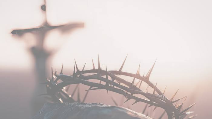 En silhuet af en tornekrone og et kors mod en rolig solnedgangshimmel.