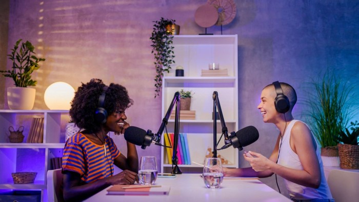Zwei Frauen sitzen in einem gut beleuchteten Raum und führen ein Podcast-Gespräch.
