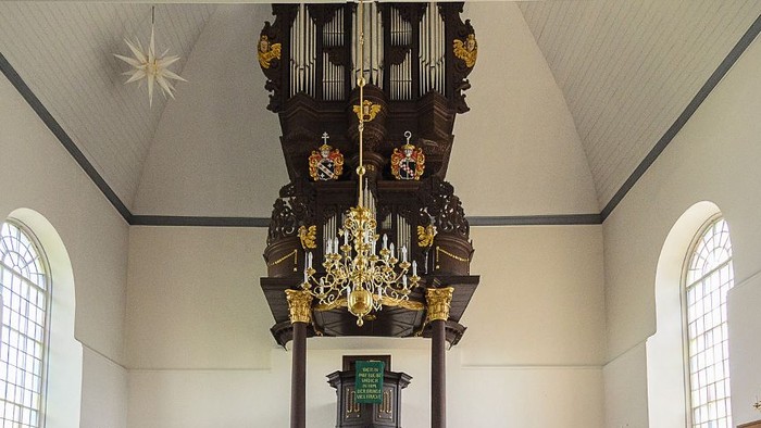 Elegante Kircheninnenausstattung mit hölzernen Kirchenbänken, prunkvoller Orgel und schlichten weißen Wänden mit Bogenfenstern.