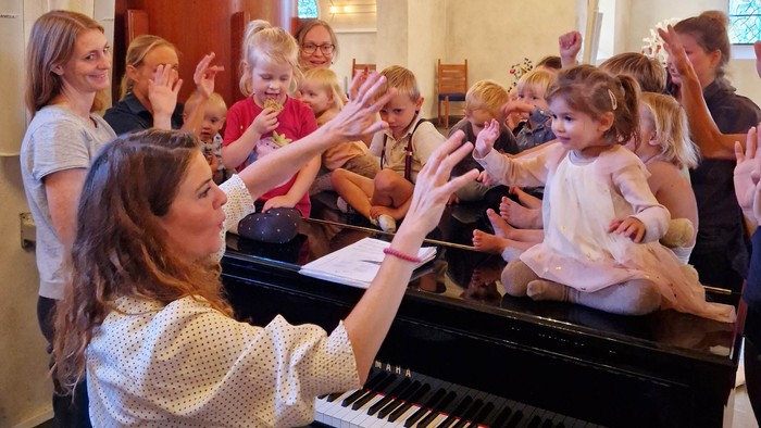 En gruppe kvinder synger i kor, mens en kvinde spiller piano