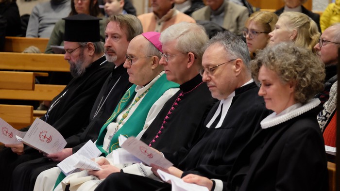En gruppe præster og præstesker i kirkeklæder sidder i en kirke.