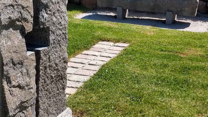 En grøn plæne med en granitbank og en mur af natursten.