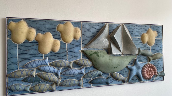 En sejlbåd på et blåt hav med fisk og skyer.