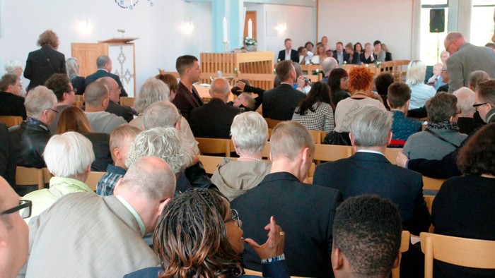 En folkemængde i en kirke, hvor folk sidder på bænke og ser fremad.