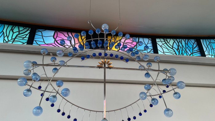 En stor hængelampe med blå lyskninger og en farverig glasvindueskærm bagved.