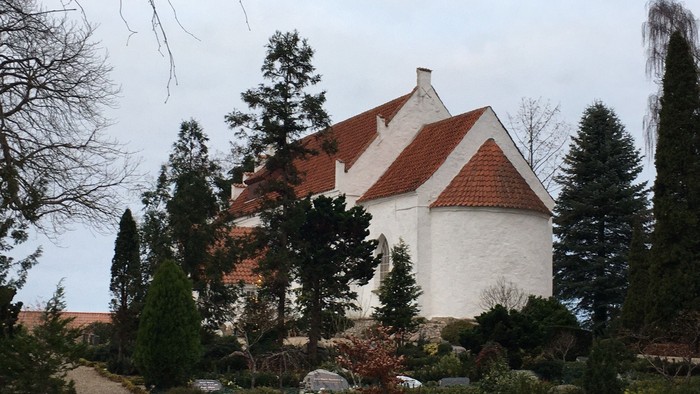 Hvid kirke med rødt tag og omgivet af træer og buske