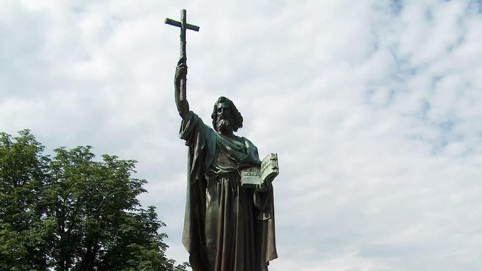 Die Statue eines Mannes mit Kreuz und Buch in einem Park