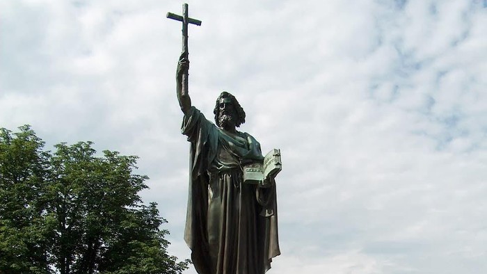 Die Statue eines Mannes mit Kreuz und Buch in einem Park