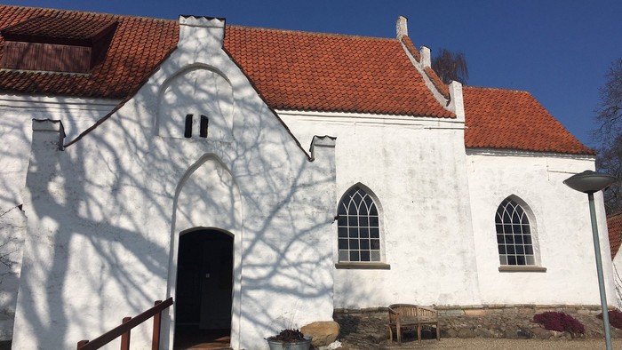Hvid kirke med rødt tag og træer, der skygger på kirkens mur