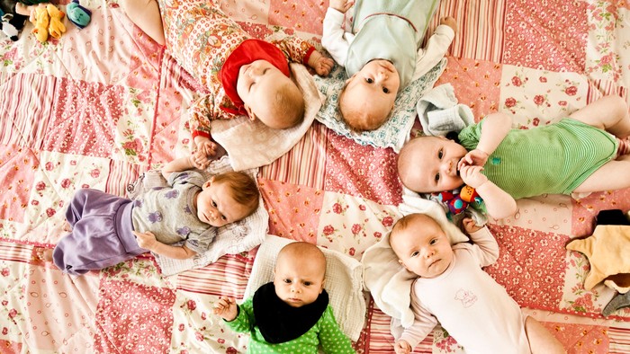 Børn og tøjpudder ligger på et blomsterbetaget sengbede.