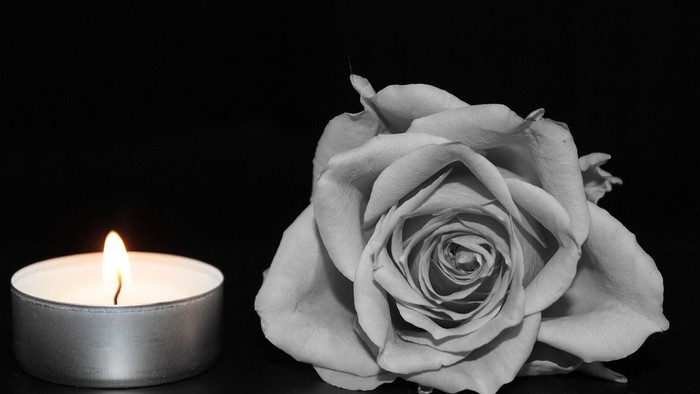 Eine brennende Kerze neben einer einzelnen Rose auf schwarzem Hintergrund