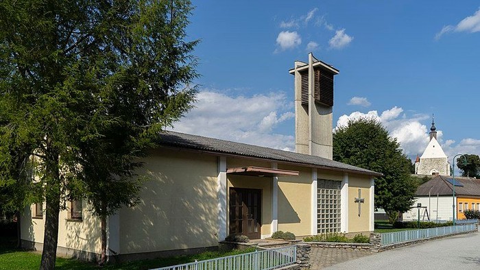 Kleine Kirche mit Glockenturm und grünem Zaun vor blauem Himmel