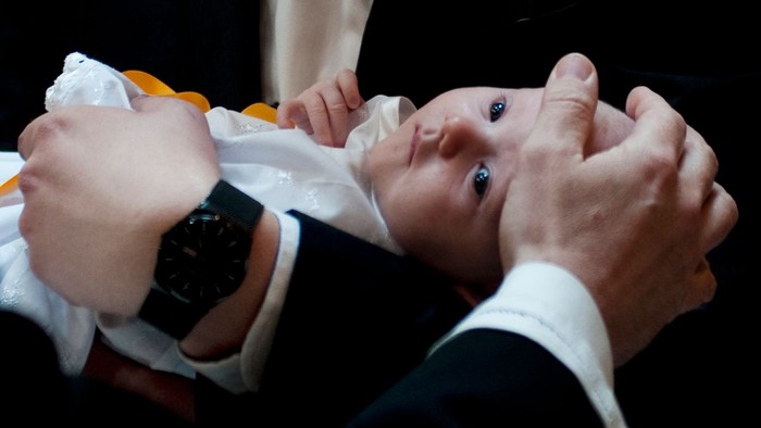 En person holder et spæd barn, der ser op og er omklædt i en hvid og gule tekstil.