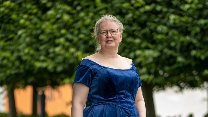 En person i en lang blå off-shoulder-kjole, der står udendørs på græsgrund.