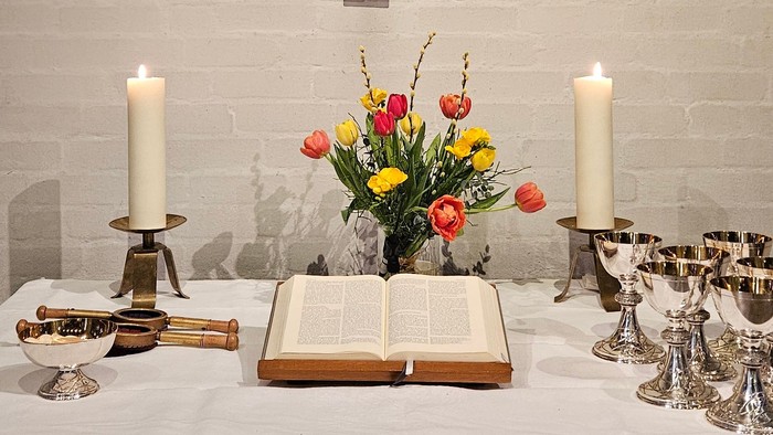 Ein Tisch mit Kerzen, Blumen und einem Buch vor einer Ziegelwand