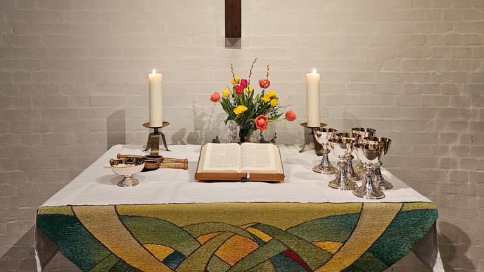 Ein Tisch mit Kerzen, Blumen und einem Buch vor einer Ziegelwand