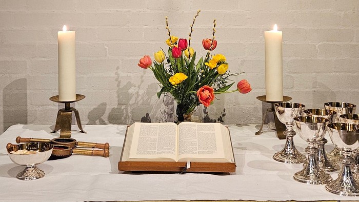 Ein Tisch mit Kerzen, Blumen und einem Buch vor einer Ziegelwand