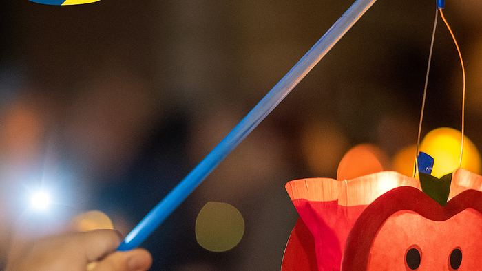 Ein Kind hält einen leuchtenden Zauberstab in der Nähe einer roten Laterne in Form eines Apfels mit einem lächelnden Gesicht.