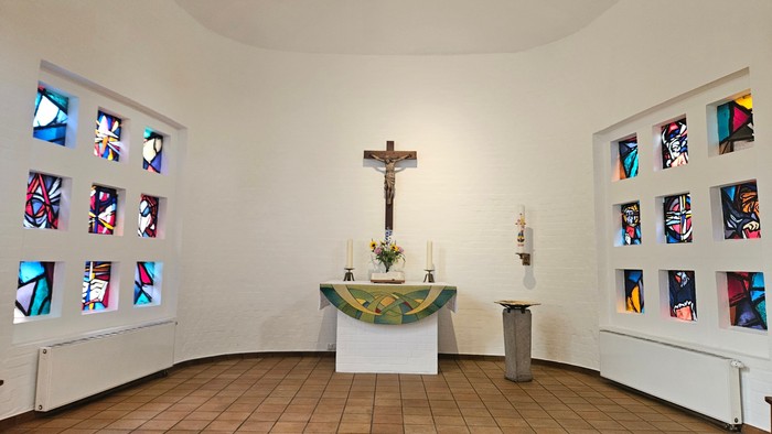 Kleine Kapelle mit farbenfrohen Fenstern und einem Altar mit Kruzifix