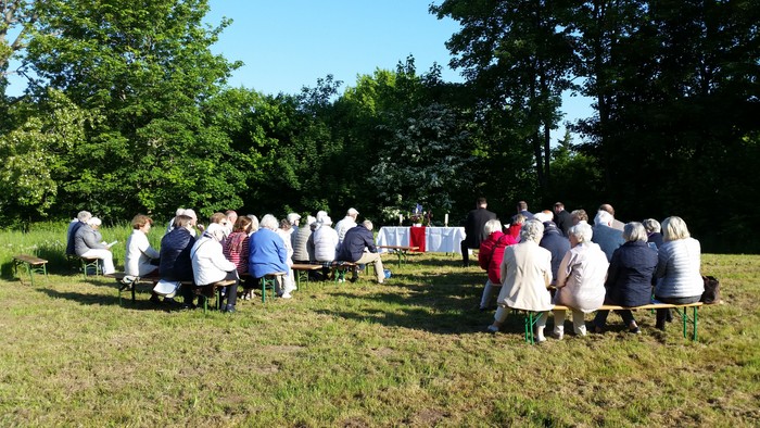 Eine Gruppe von Menschen sitzt im Freien auf Stühlen und hört einem Redner zu.