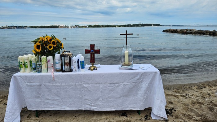 Ein Tisch am Strand mit Blumen, Kerzen und Kreuzen