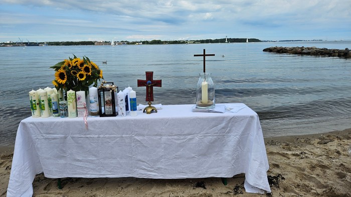 Ein Tisch am Strand mit Blumen, Kerzen und Kreuzen