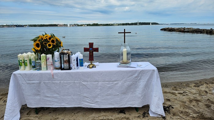 Ein Tisch am Strand mit Blumen, Kerzen und Kreuzen