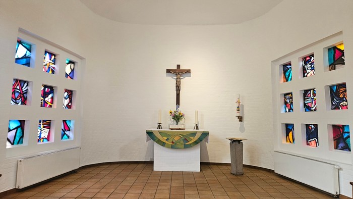 Kleine Kapelle mit farbenfrohen Fenstern und einem Altar mit Kruzifix
