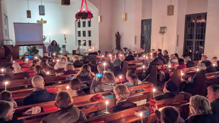 Ein überfüllter Hörsaal mit Teilnehmern, die während einer Abendveranstaltung oder Zeremonie Kerzen halten.