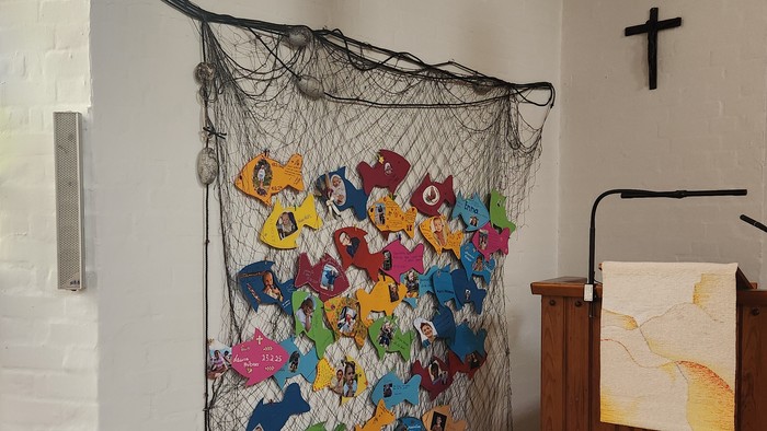 Bunte Papierschnitte an einem Netz in einem Raum mit Kreuz und Bücherregal