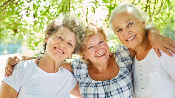 Drei glückliche ältere Frauen umarmen sich unter einem Baum