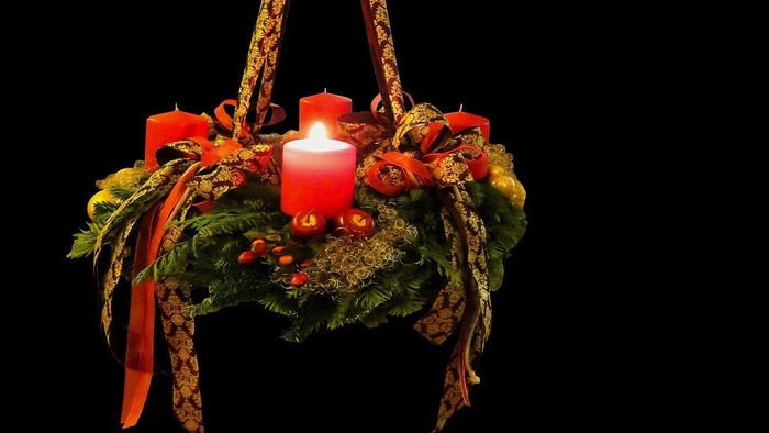 Ein Adventskranz mit brennender Kerze hängt an einem dunklen Hintergrund