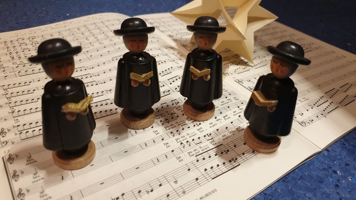 Fünf hölzerne Figurinen mit schwarzen Hüten und Fliegen auf Notenblättern.